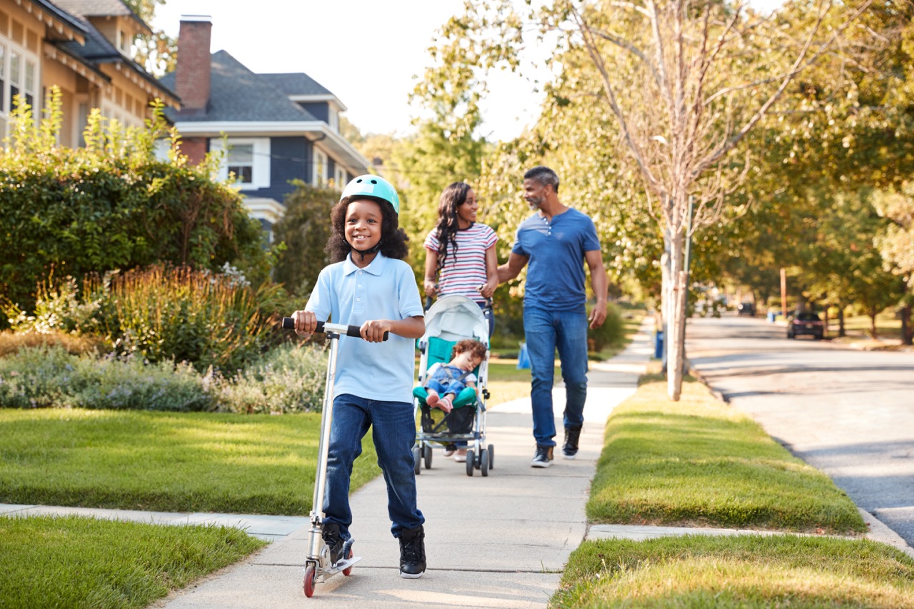 A family walking along a tree-lined neighborhood sidewalk